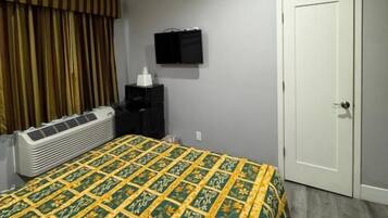 Una habitación de hotel con una cama, televisión, aire acondicionado y una puerta.