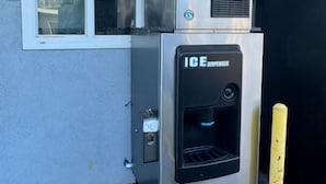An outdoor ice dispenser attached to a building's exterior wall, with a window above it. - Moonlight Inn (Gardena)