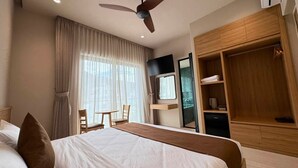Habitación de hotel con cama, escritorio, silla, televisión, armario y ventilador de techo.