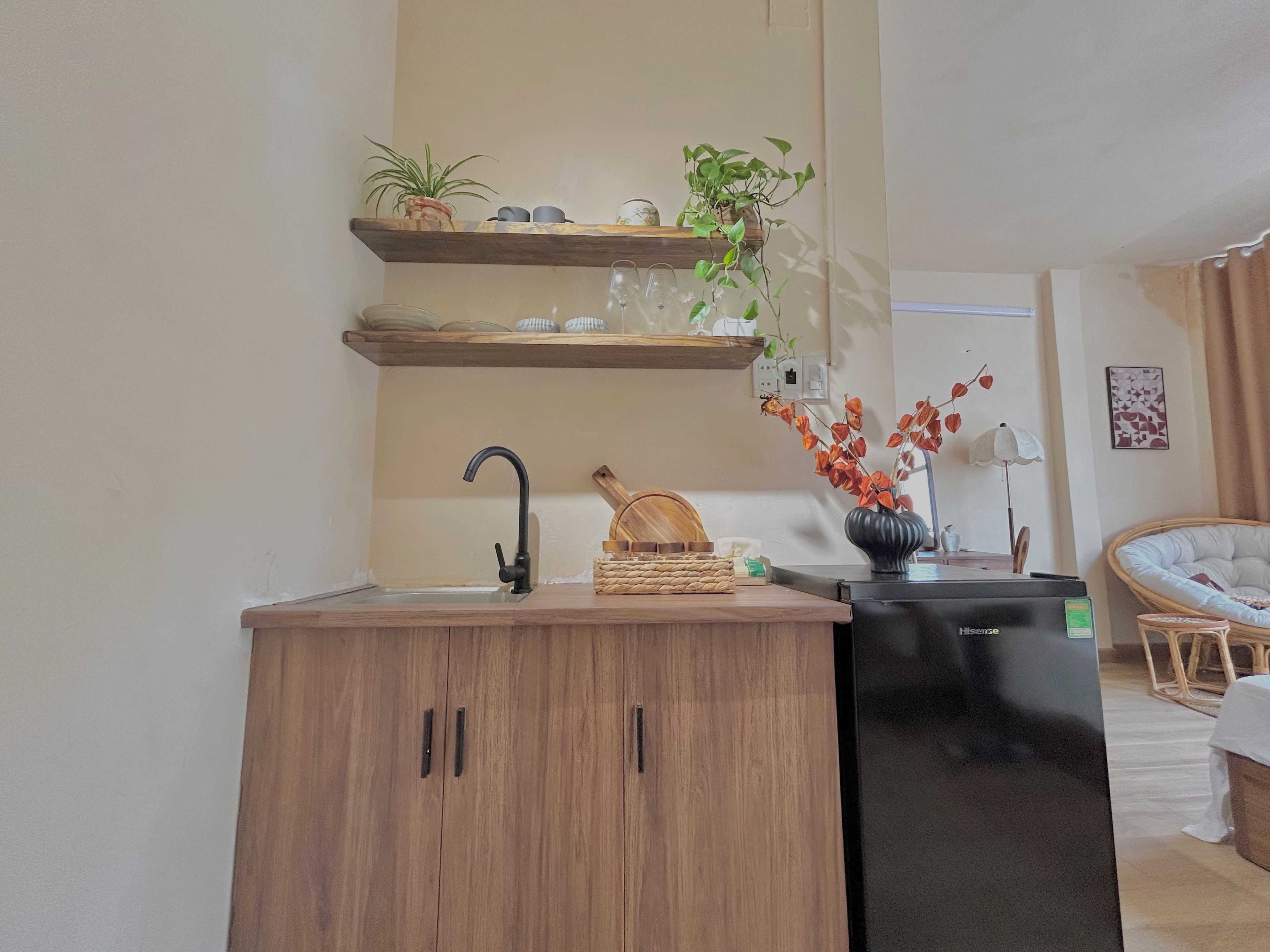 Una cocina compacta con lavamanos, armarios de madera, un refrigerador negro y una zona de comedor con una silla y una mesa.