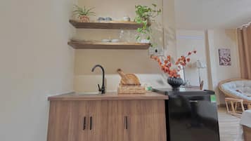 A compact kitchen with a sink, wooden cabinets, a black refrigerator, and a dining area with a chair and table.