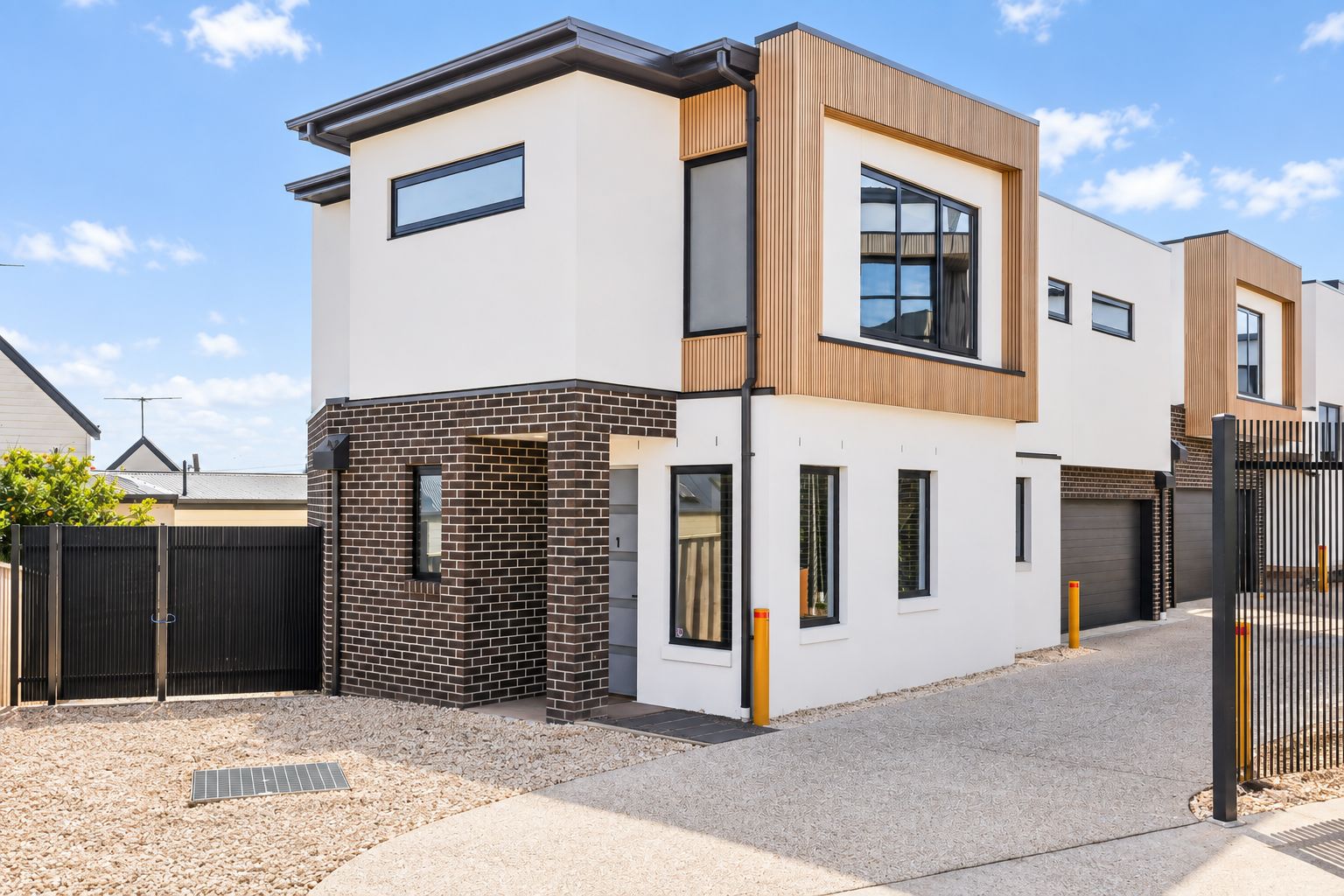 Une maison moderne à deux étages, avec une façade en briques, de grandes fenêtres et une allée d’accès fermée par un portail.