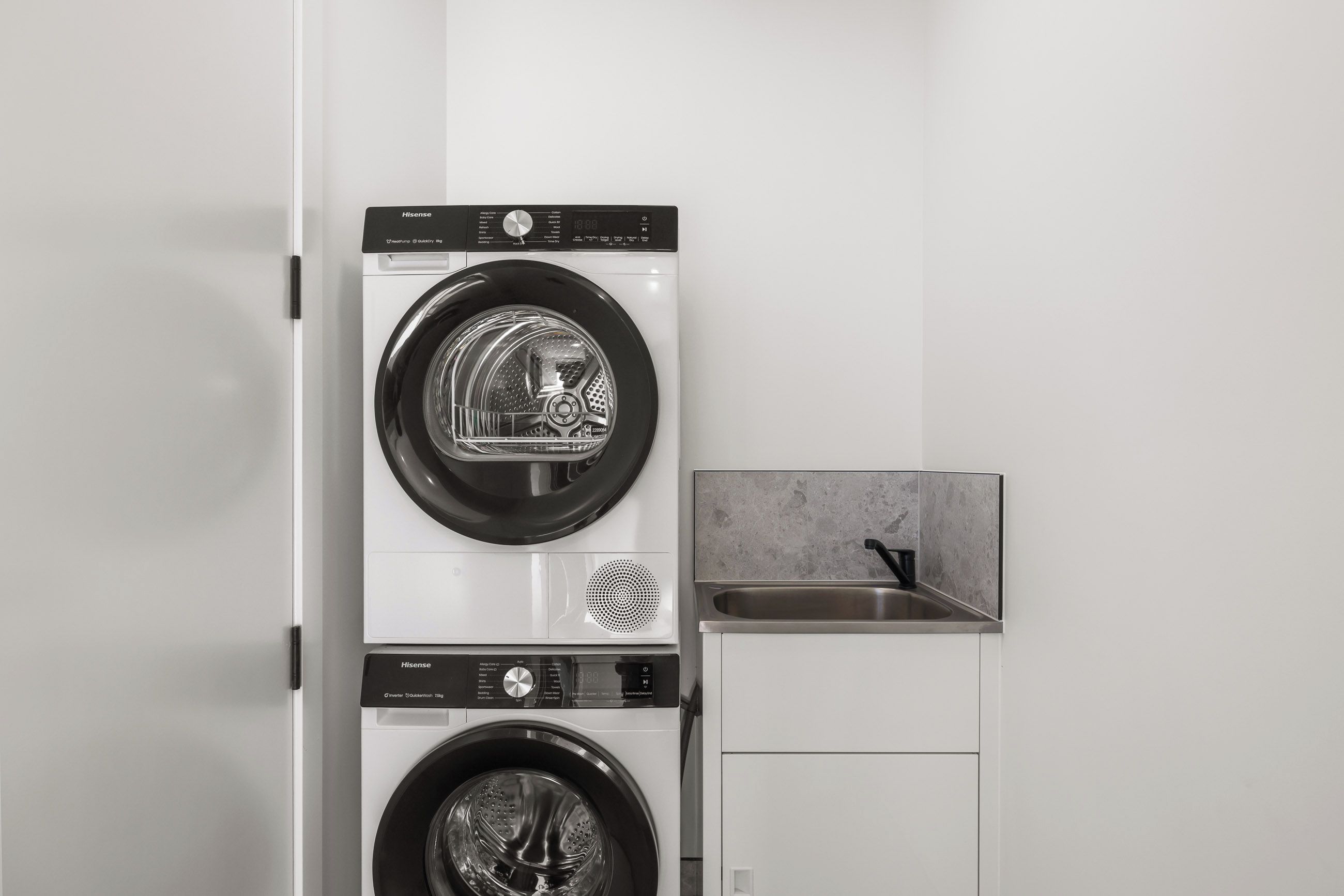 A compact, wall-mounted laundry unit with two washing machines, a control panel, and a small sink.