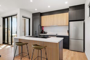Une cuisine moderne dotée d’un îlot central, d’appareils électroménagers en acier inoxydable et offrant une vue sur l’extérieur.