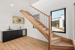 A modern kitchen with a wooden staircase, a black countertop, and a window with a view of the outside. - Longfin Cove - Villa 1 by Ready Set Stay (San Remo)