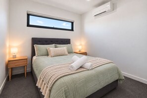 Un lit bien fait, avec une tête de lit, deux lampes de chevet, une fenêtre et un appareil de climatisation.
