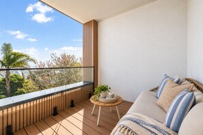 A balcony with a wooden floor, a sofa, and a small round table with a plant. - Longfin Cove - Villa 1 by Ready Set Stay (San Remo)