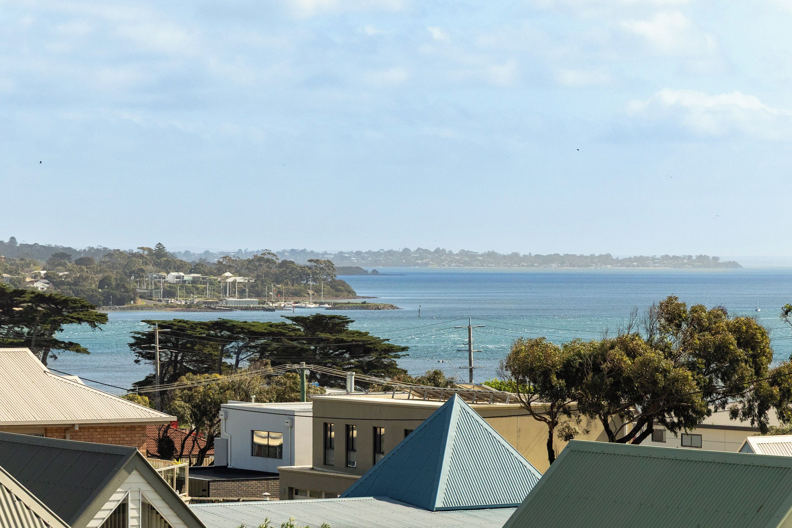 A coastal residential area with houses, a clear sky, and a view of the sea.