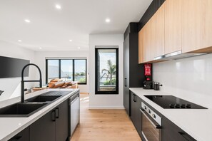 A modern kitchen with a central island, black cabinets, and a view to a balcony. - Longfin Cove - Villa 1 by Ready Set Stay (San Remo)