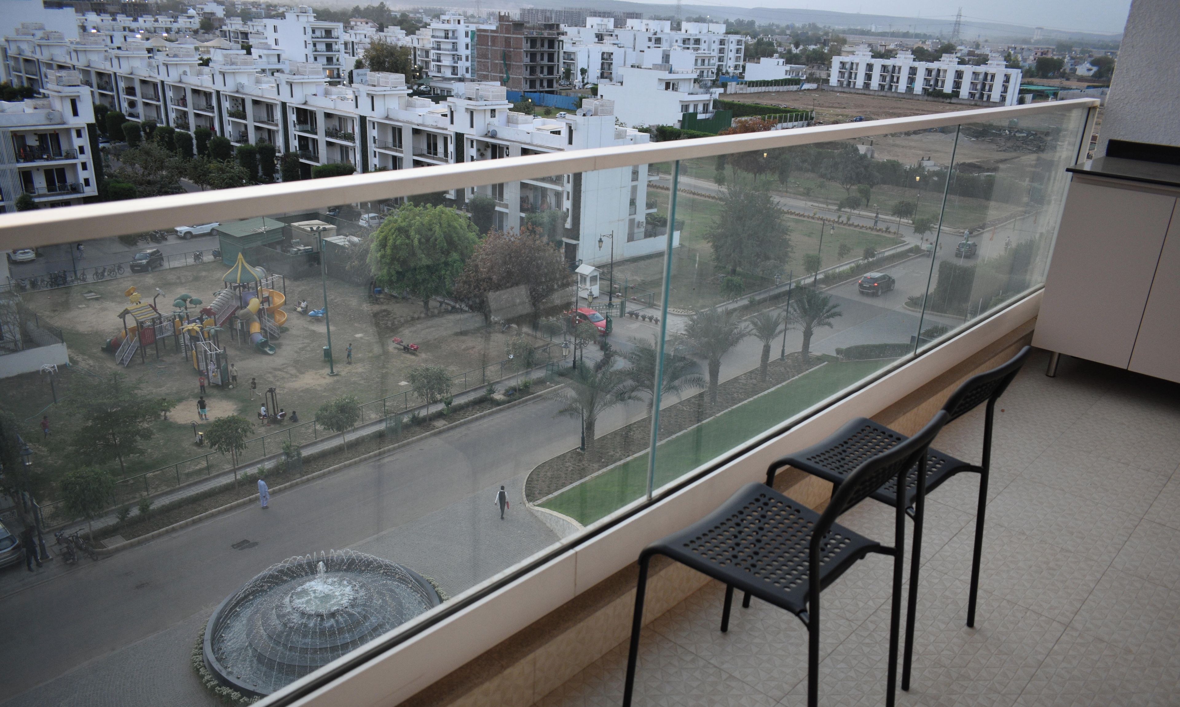 A balcony with a view of a residential area, a playground, and a fountain.