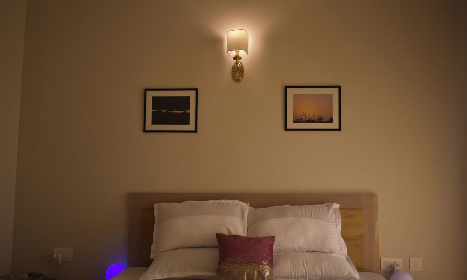 A hotel room with a bed, two framed pictures on the wall, and a wall-mounted lamp.