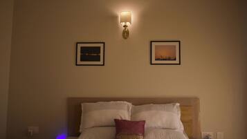 A hotel room with a bed, two framed pictures on the wall, and a wall-mounted lamp.