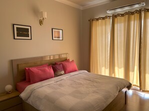 Ein Schlafzimmer mit einem Bett, einem Nachttisch, einer Wandleuchte und einem Fenster mit Vorhängen.