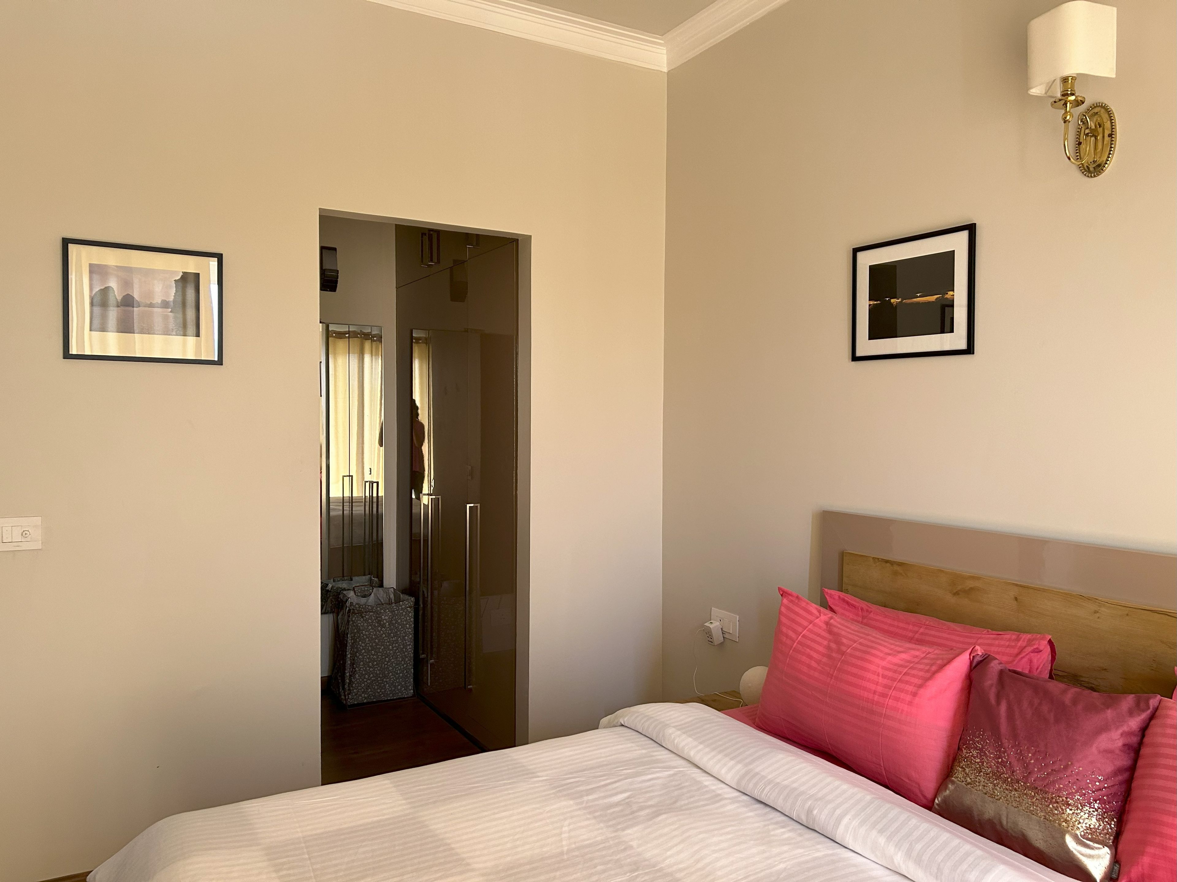 A hotel room with a bed, a nightstand, a wall-mounted lamp, and a door leading to a bathroom.