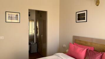 A hotel room with a bed, a nightstand, a wall-mounted lamp, and a door leading to a bathroom.