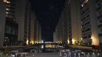 A nighttime view of a hotel corridor with multiple floors, outdoor seating, and a pool area.