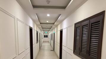 A long, narrow hotel corridor with doors on both sides, a tiled floor, and a ceiling with recessed lighting.