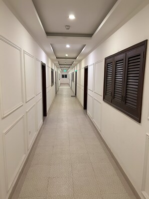Passadís llarg i estret d'un hotel, amb portes a ambdós costats, terra enrajolada i sostre amb il·luminació empotrada.