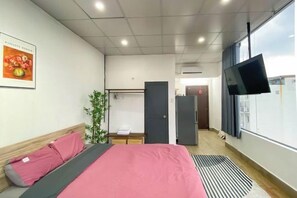 A hotel room with a bed, a flat-screen TV, a wardrobe, and a window. - Zeus Living - Cozy Apartment in Thao Dien (Ho Chi Minh City)
