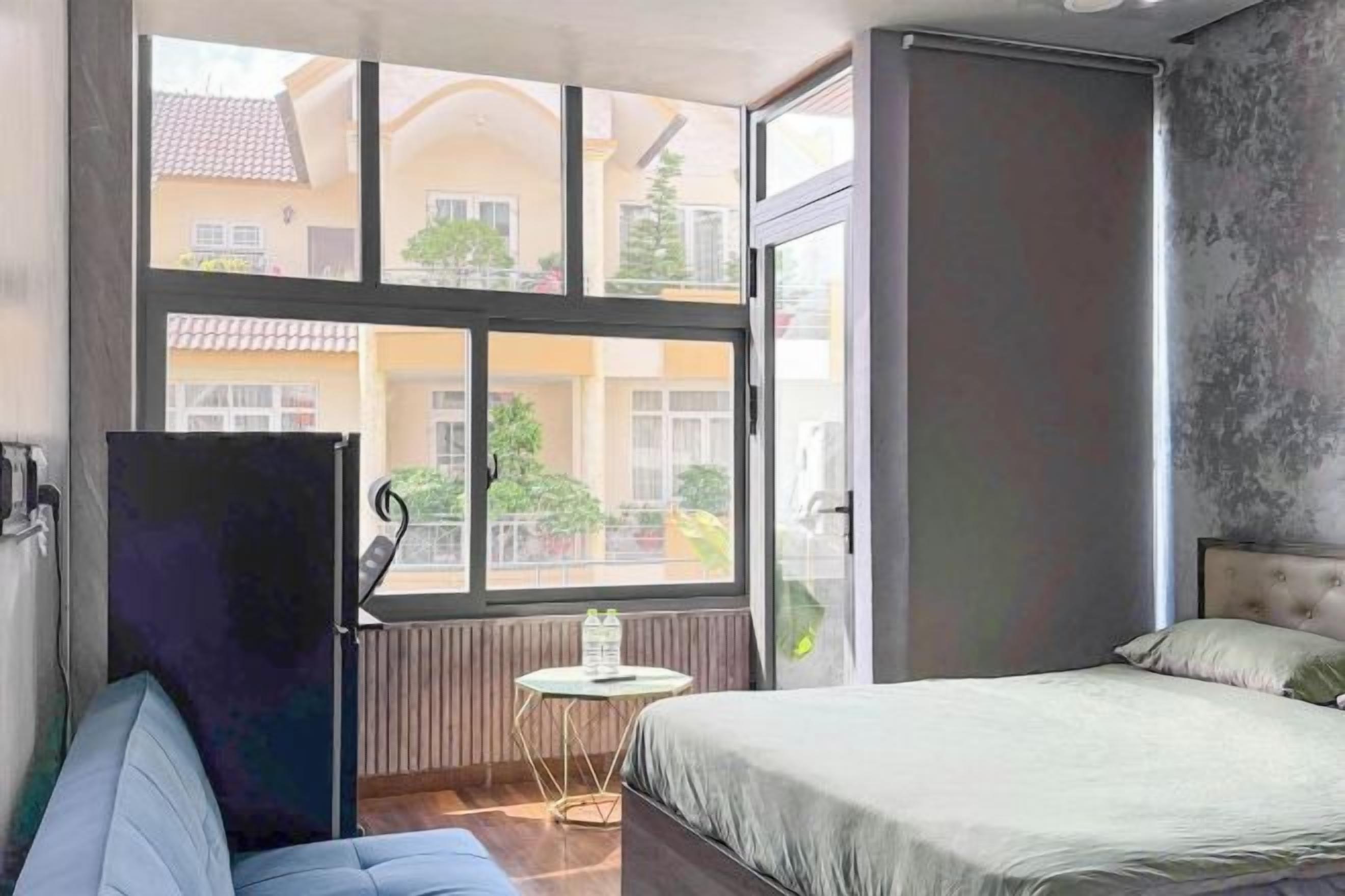 Ein Schlafzimmer mit einem Bett, einem kleinen Tisch und einem Fenster mit Blick auf Gebäude.