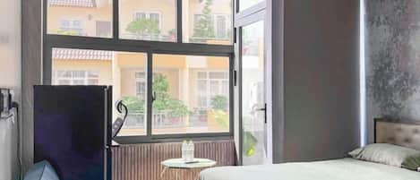 Un dormitorio con cama, una mesita y una ventana con vistas a edificios.