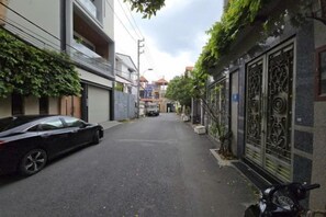 Eine schmale Straße mit parkenden Autos und einem Motorrad, Gebäude mit Metallgittern und einem wolkenlosen Himmel.