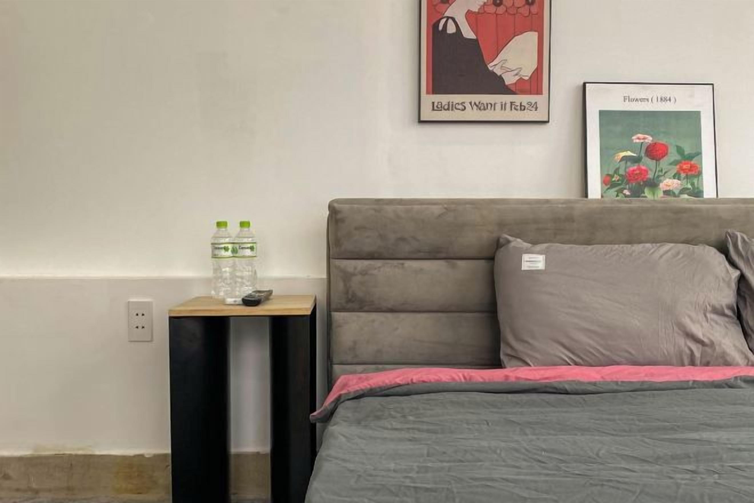Une chambre à coucher avec un lit, une table de chevet, un tableau encadré et une prise de courant au mur.
