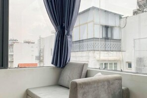 Ein Eckzimmer mit Fenster, einem Sessel und Blick auf ein Gebäude.