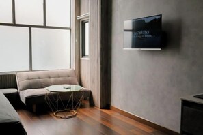 A modern living room with a sofa, a small round table, and a flat-screen TV mounted on the wall. - Zeus Living - Cozy Apartment in Thao Dien (Ho Chi Minh City)