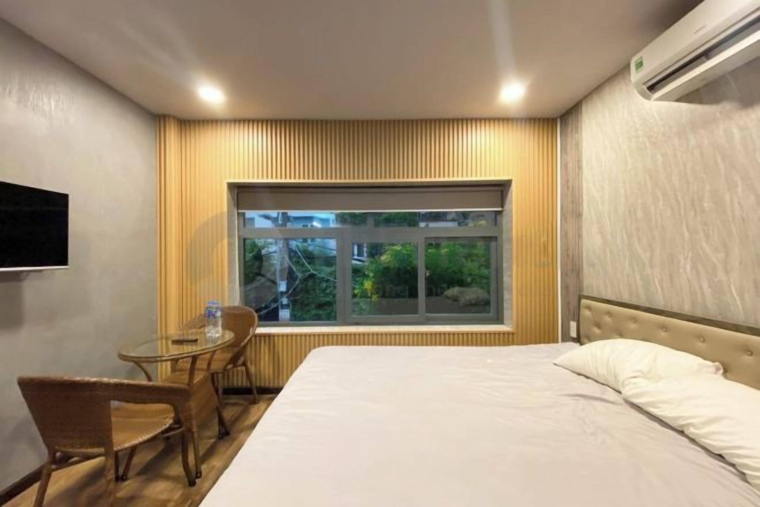 Une chambre d’hôtel avec un lit, une petite table avec des chaises, une fenêtre donnant sur un paysage agréable et un appareil de climatisation.
