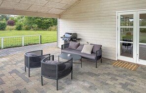 Un patio exterior con una parrilla, asientos y vistas a un área verde.