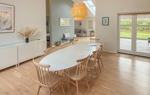 Un comedor moderno con una mesa blanca y sillas de madera, una lámpara colgante y vistas a un jardín a través de un ventanal.