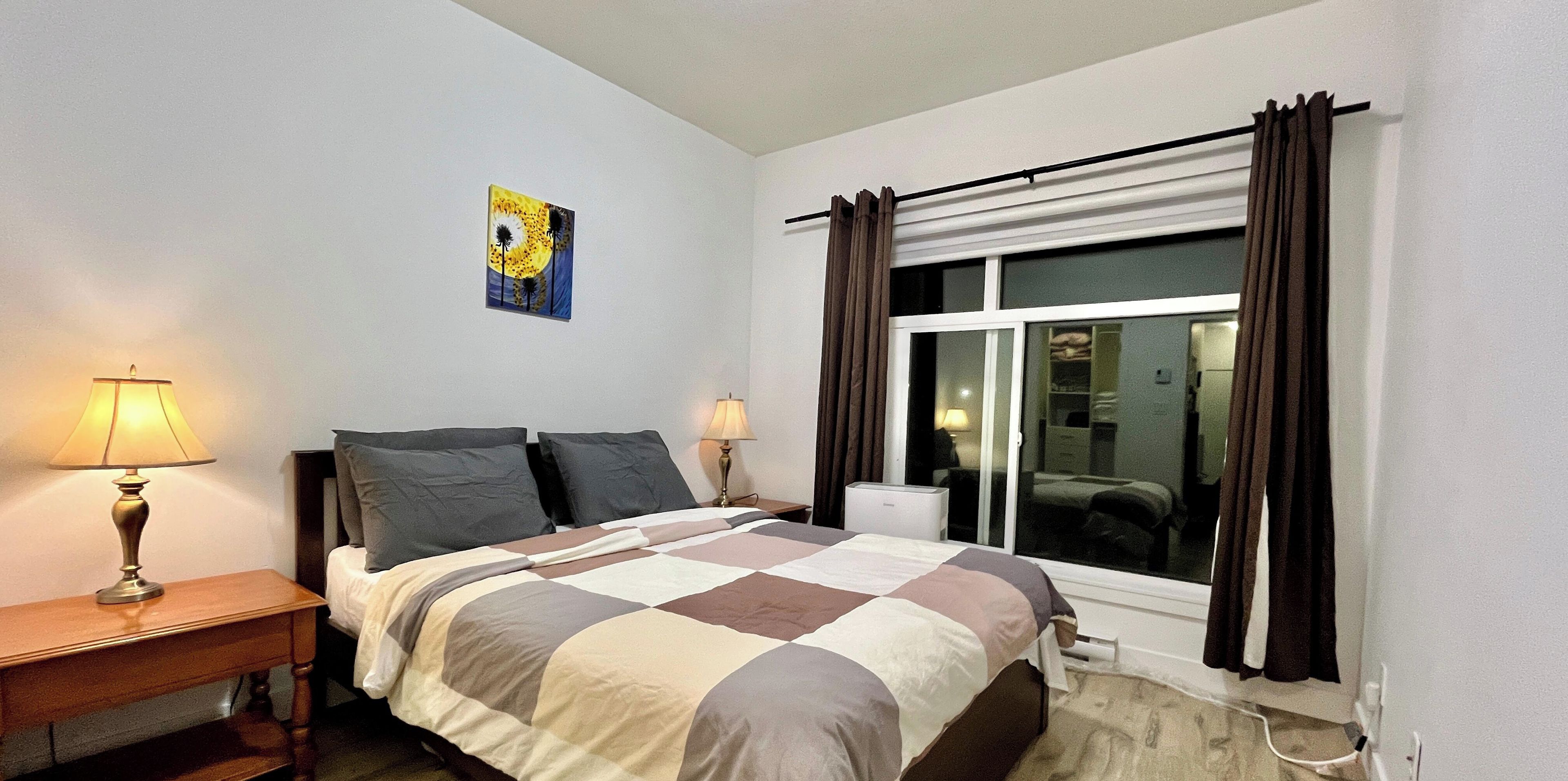 Un dormitorio con cama, dos lámparas de noche, una ventana con cortinas y un cuadro en la pared.