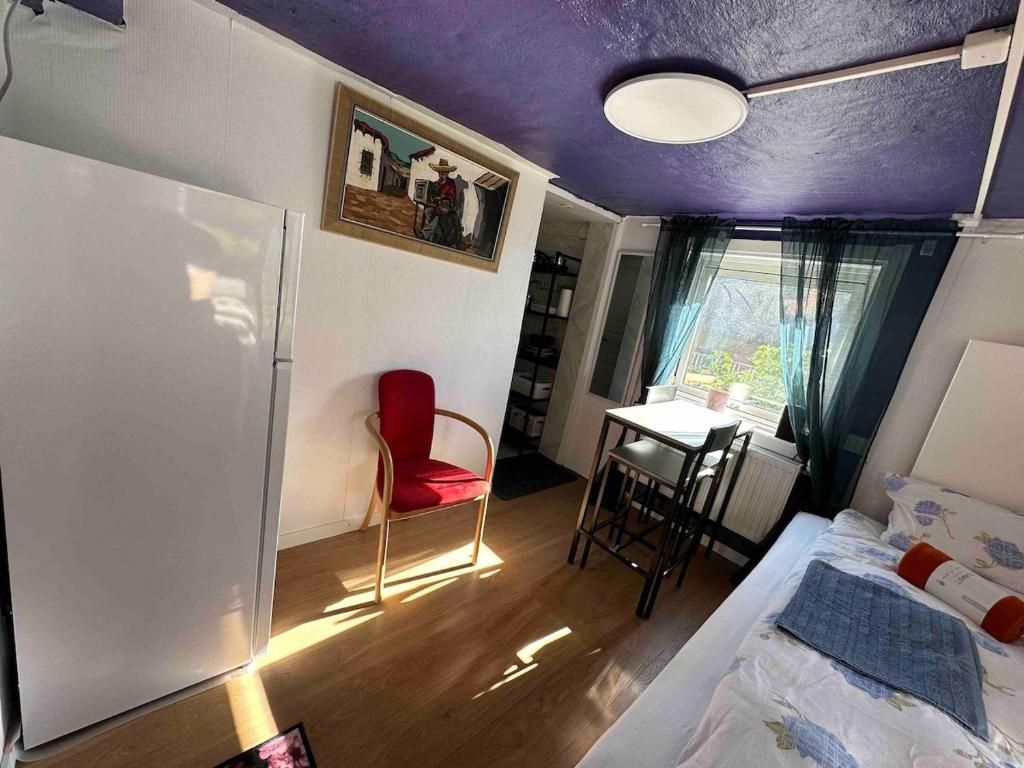 Une petite pièce comprenant un lit, un bureau, une chaise, un réfrigérateur et une fenêtre avec des rideaux.
