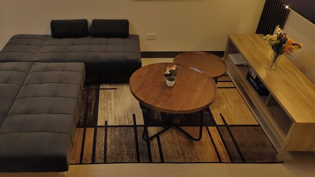 Un salon moderne avec un canapé d’angle, une table basse ronde en bois et un buffet agrémenté d’un vase de fleurs.