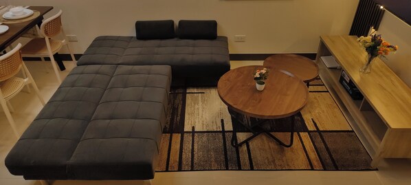 Una sala moderna con un sofá modular, una mesa de centro redonda de madera y un aparador con un jarrón de flores.