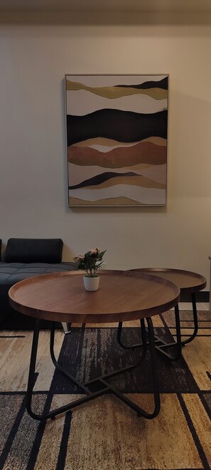 A room with a round wooden table, a black sofa, and a large abstract painting on the wall. - Spacious Family-Friendly 2BR Near BGC & McKinley! (Pasig)