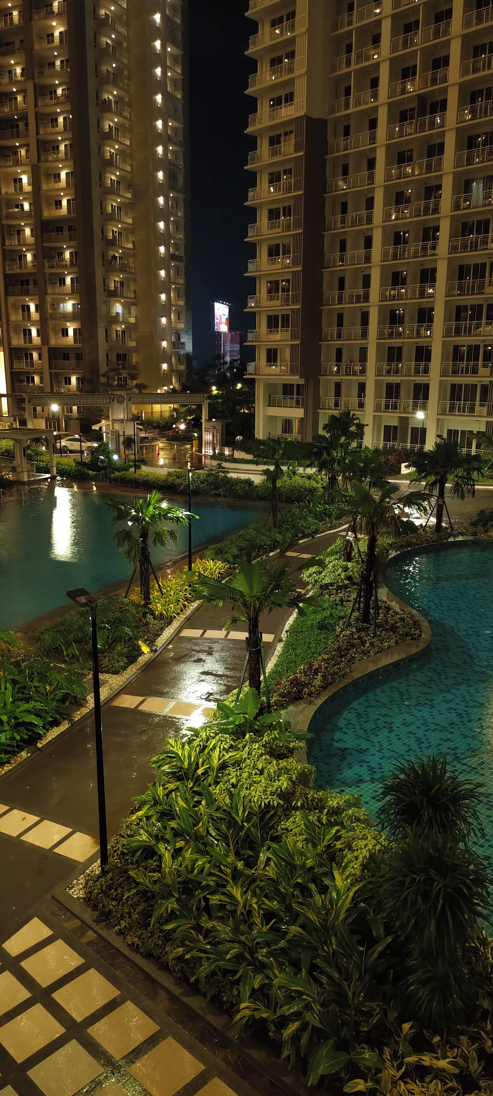 A nighttime view of a hotel with multiple high-rise buildings, a swimming pool area with water features, and well-maintained landscaping.