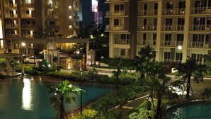 Une vue nocturne d’un hôtel composé de plusieurs immeubles de grande hauteur, avec un espace piscine agrémenté de jeux d’eau et des jardins paysagers bien entretenus.