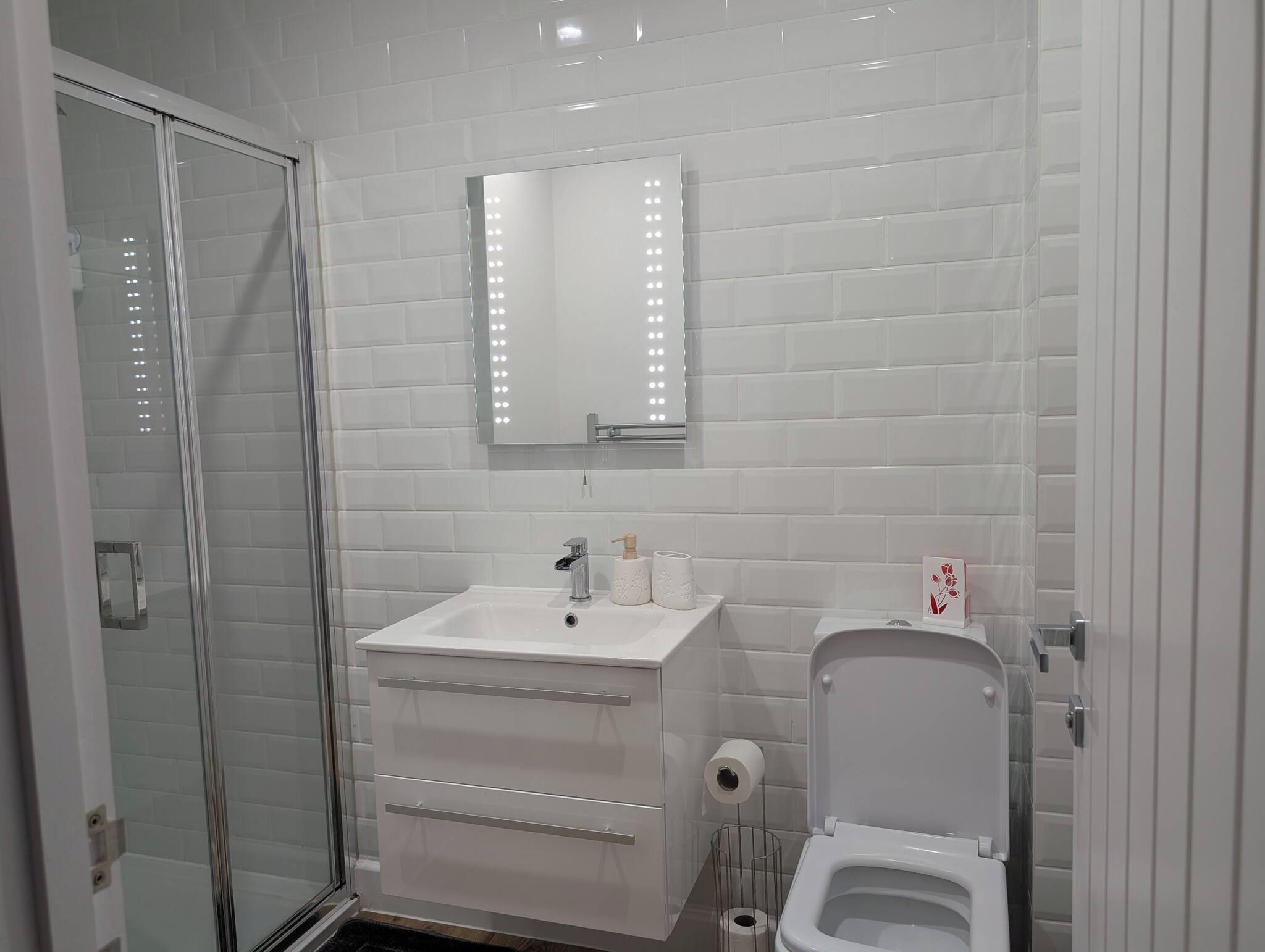 Een badkamer met een douchecabine van glas, een wit wastafelmeubel met spiegel en een toilet met handdoekhouder.