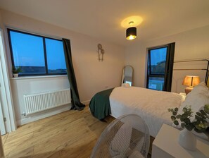 Ein Hotelzimmer mit Bett, Fenster, Heizkörper, Spiegel, Lampe und Pflanze.