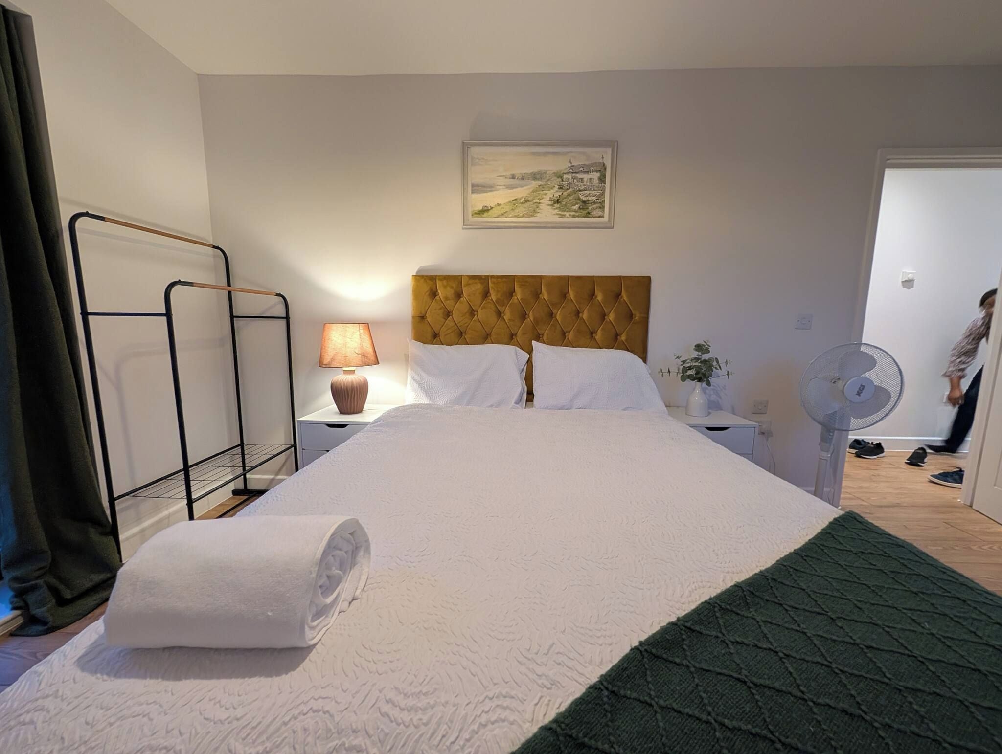 Quarto de hotel com cama grande, abajur, ventilador e quadro na parede.