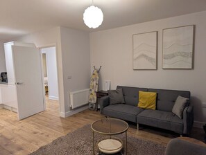 A modern living room with a grey sofa, a round coffee table, and a white door leading to another room.