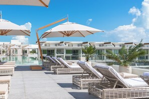 Un área de piscina en la azotea con sillas de descanso y sombrillas.