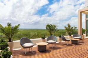Una terraza de madera con mobiliario exterior, plantas en macetas y vistas al paisaje.