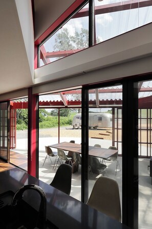 A modern interior with large windows, a dining area with chairs and a table, and a view of an outdoor area with a trailer. - A Private Villa Nestled Among the Fields of Biei | Accommodates up to 12 Guests—Enjoy BBQs and Bonfires at Villa Hokuto (Kitami)