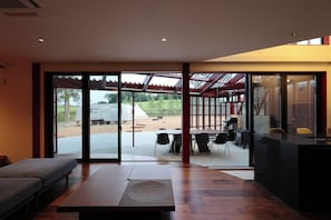 A modern interior with a large sliding glass door leading to an outdoor area, a seating area with a bench, and a dining space with tables and chairs. - A Private Villa Nestled Among the Fields of Biei | Accommodates up to 12 Guests—Enjoy BBQs and Bonfires at Villa Hokuto (Kitami)