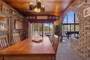A dining area with a long wooden table, chairs, a chandelier, and a piano in the background. - Luxury Waterfront Retreat with Private Pool (Daleys Point)