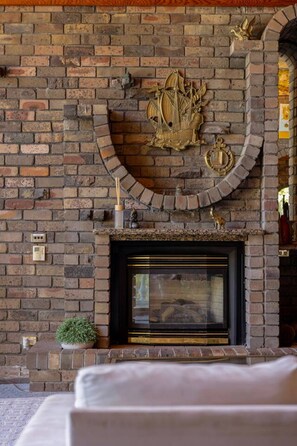A brick fireplace with a decorative ship and compass, a small potted plant, and a wall-mounted thermostat. - Luxury Waterfront Retreat with Private Pool (Daleys Point)