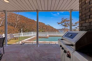 A covered patio with a grill, a pool, and a view of a hilly landscape. - Luxury Waterfront Retreat with Private Pool (Daleys Point)